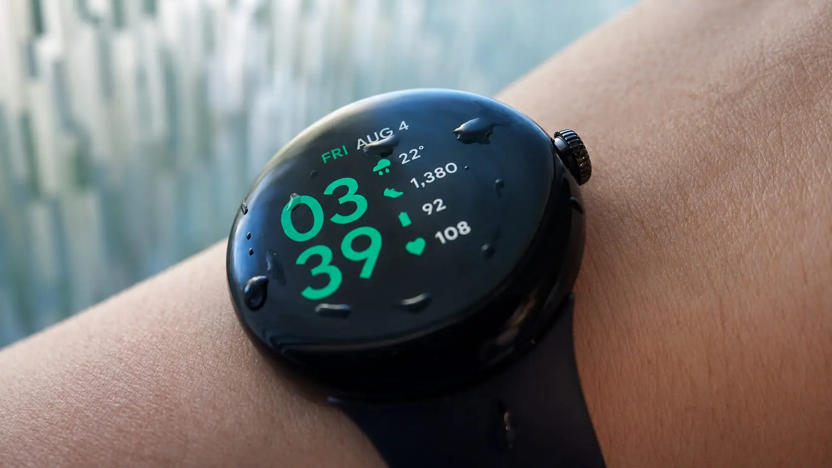 ساعة Google Pixel Watch 5 سوداء اللون على المعصم مع قطرات ماء على الشاشة في صورة ترويجية توضح تصميم الساعة الذكية.